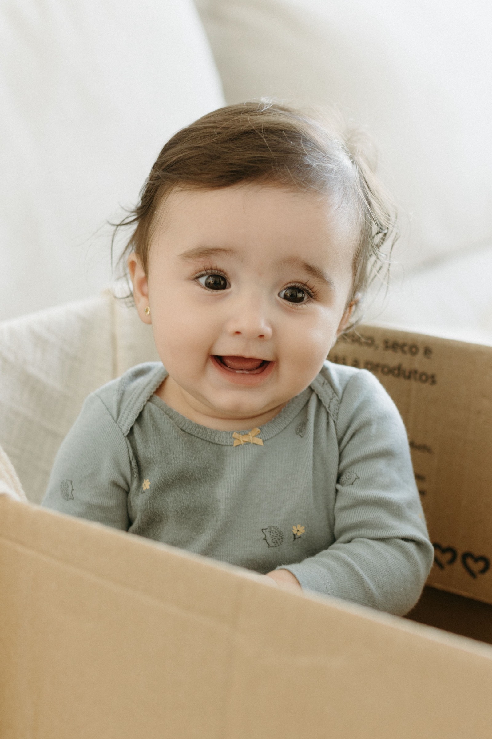 A happy baby peeking out of a cardboard box