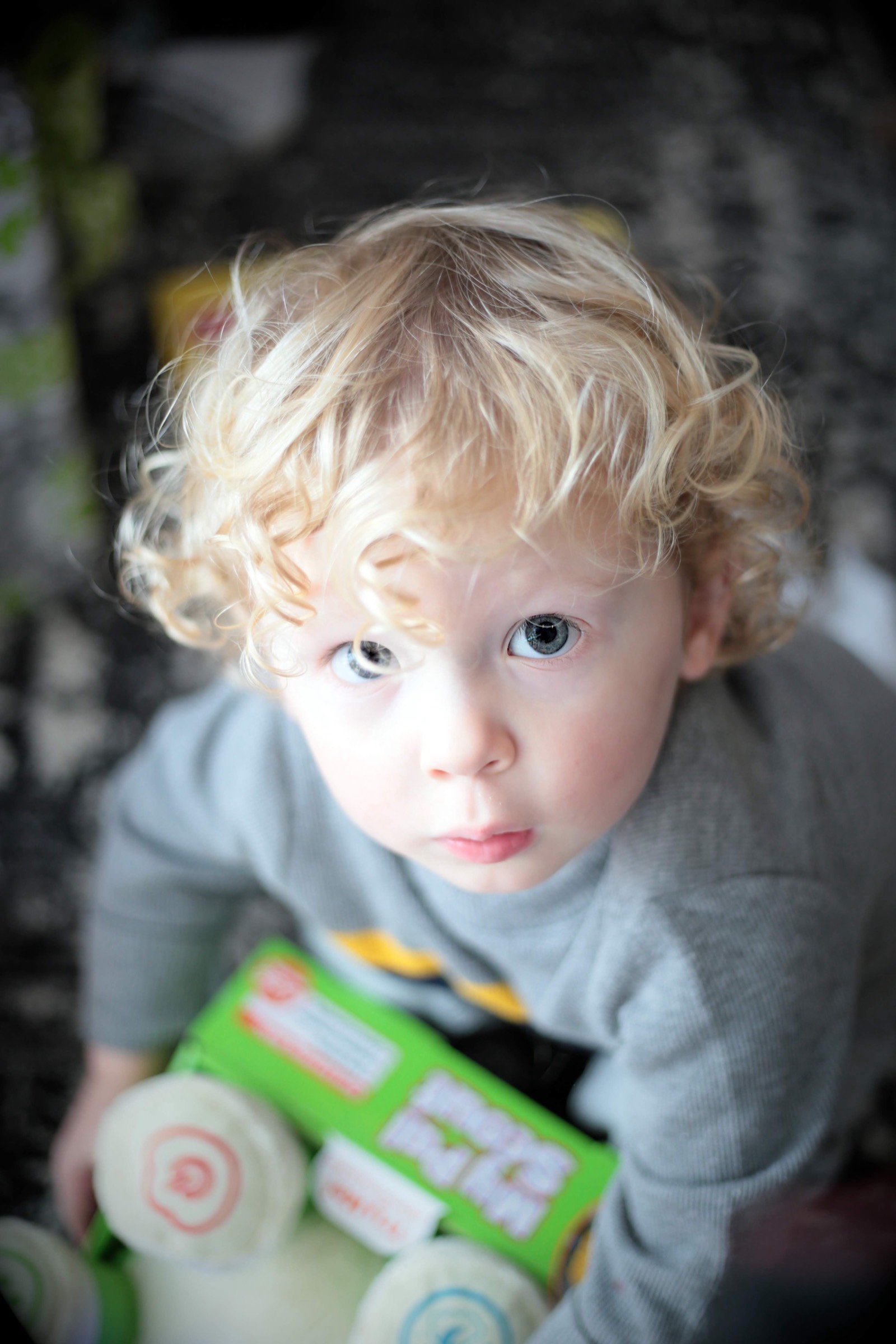 A curly-haired toddler holding a toy and looking up